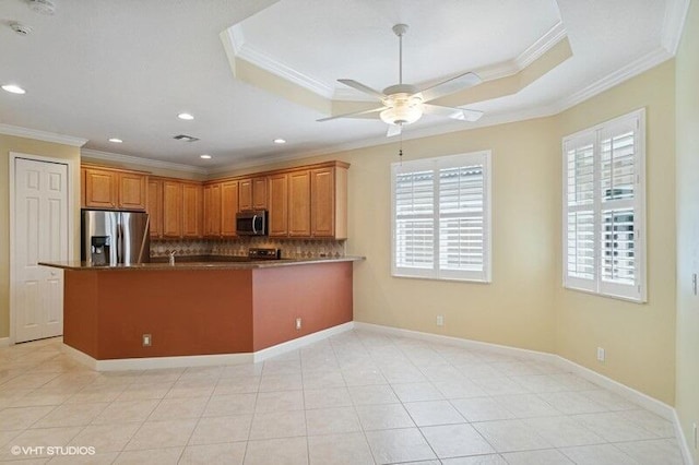 kitchen with a tray ceiling, appliances with stainless steel finishes, ornamental molding, and decorative backsplash