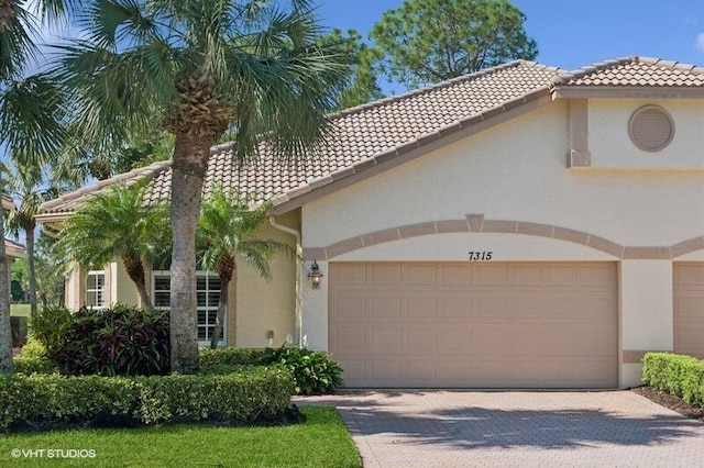 mediterranean / spanish-style house featuring a tiled roof, stucco siding, an attached garage, and driveway