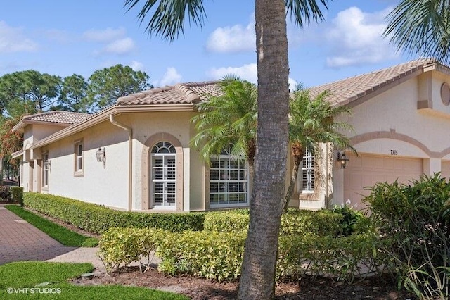 view of side of property with stucco siding, a tiled roof, and a garage