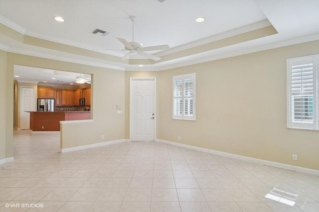 empty room with a ceiling fan, baseboards, visible vents, a tray ceiling, and ornamental molding