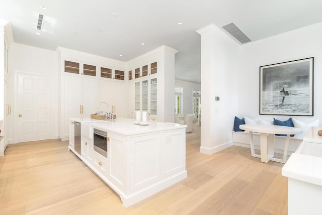 205 Gray St, West Palm Beach, FL 33405 - kitchen featuring light wood finished floors, white cabinetry, light countertops, glass insert cabinets, and an island with sink