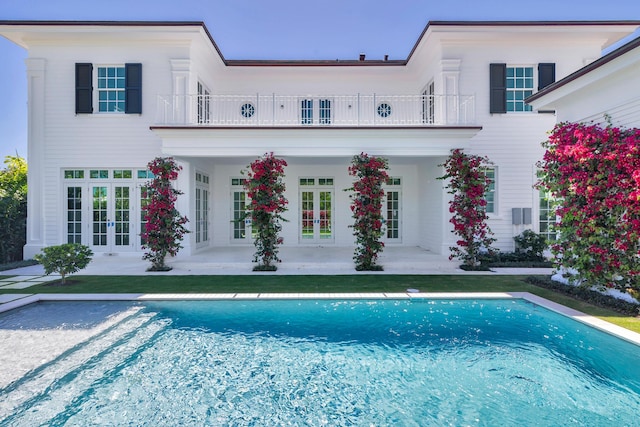 back of property featuring an outdoor pool, french doors, a balcony, and a patio area