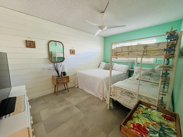 bedroom with wooden walls, a textured ceiling, and ceiling fan