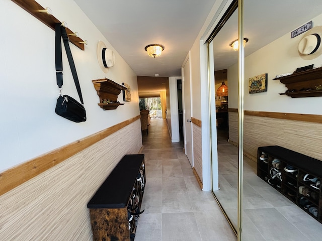 hallway featuring light tile patterned floors, wainscoting, and tile walls