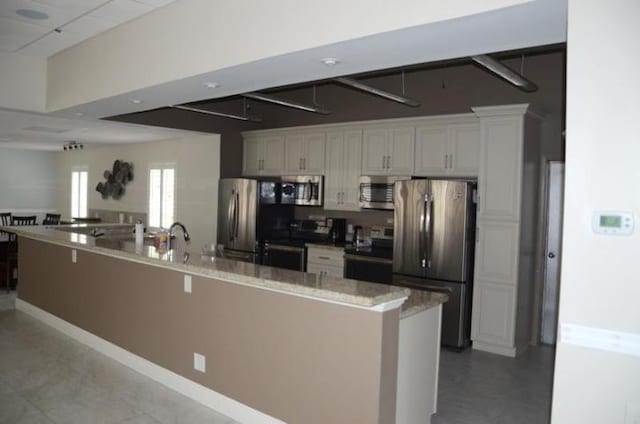 kitchen with a spacious island, light stone countertops, a breakfast bar, appliances with stainless steel finishes, and white cabinets