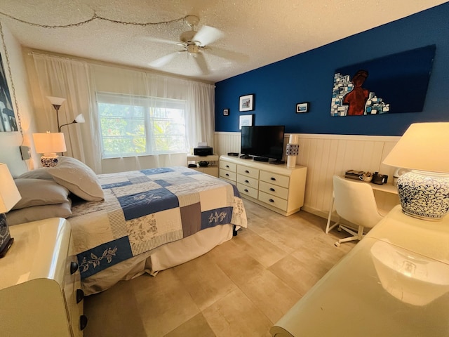 bedroom featuring a wainscoted wall, a textured ceiling, and ceiling fan