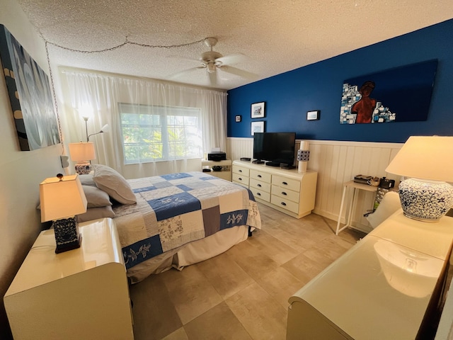 bedroom featuring a ceiling fan, a textured ceiling, and wainscoting