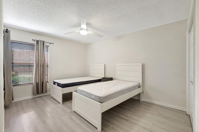 bedroom with a textured ceiling, light wood-style floors, baseboards, and ceiling fan