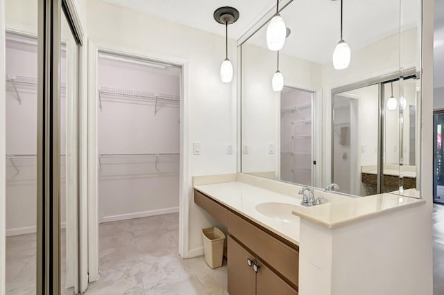 bathroom with vanity, a walk in closet, baseboards, and marble finish floor