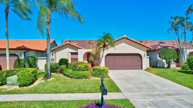 mediterranean / spanish home featuring stucco siding, driveway, a front yard, a garage, and a tiled roof