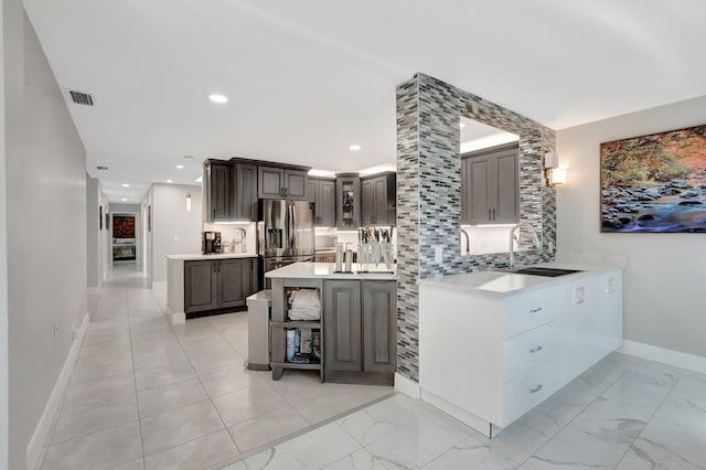 kitchen featuring visible vents, light countertops, decorative backsplash, stainless steel fridge, and a sink