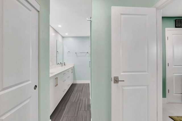 full bath with double vanity, wood finish floors, baseboards, and a sink