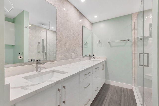 bathroom with a sink, baseboards, a stall shower, and double vanity