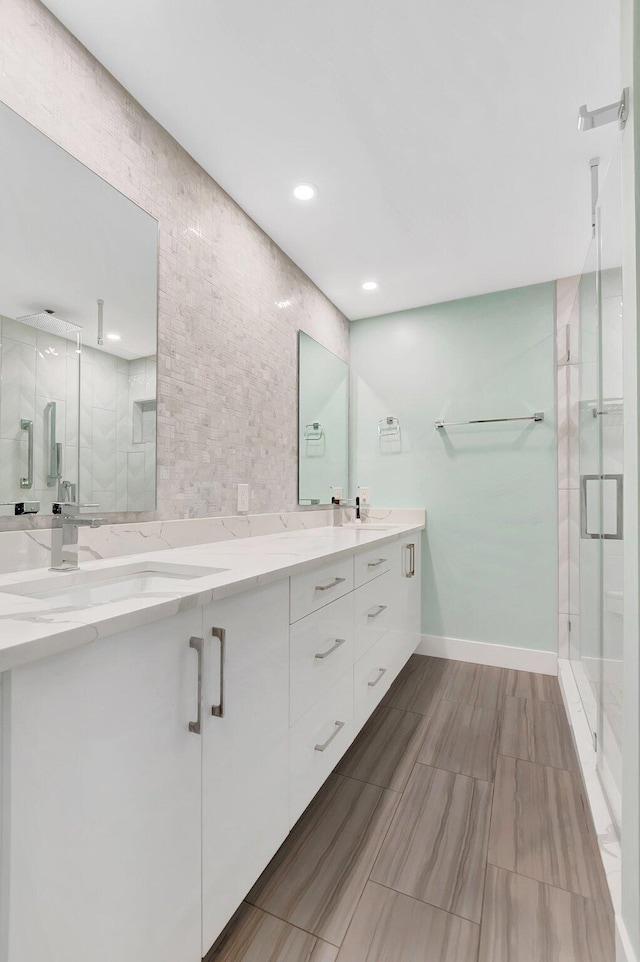 bathroom with double vanity, baseboards, a shower stall, and a sink