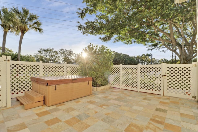 view of patio with a gate, a hot tub, and fence