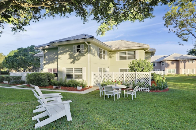 rear view of house featuring stucco siding, fence, a lawn, and a tiled roof