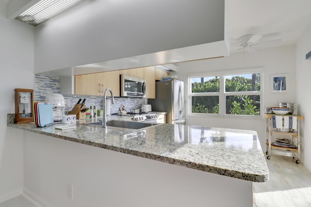kitchen with backsplash, light brown cabinets, light stone counters, appliances with stainless steel finishes, and a sink