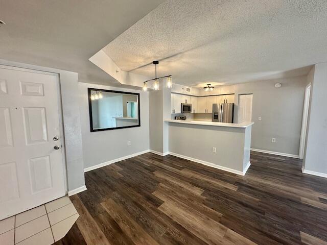 7896 Sonoma Springs Cir Unit 204, Lake Worth, FL 33463 - kitchen featuring a peninsula, dark wood-style flooring, stainless steel appliances, light countertops, and a textured ceiling