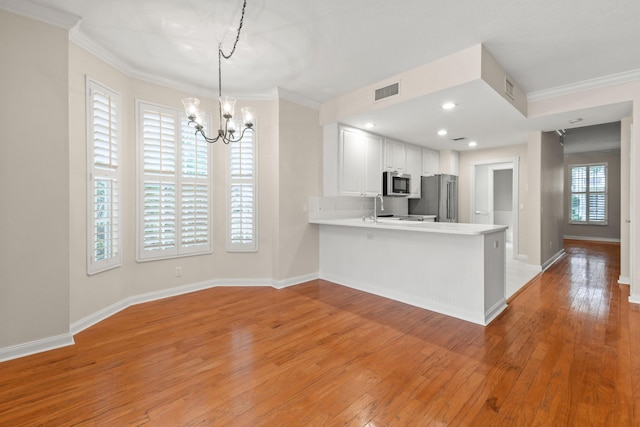 kitchen featuring appliances with stainless steel finishes, light wood-type flooring, a peninsula, and ornamental molding