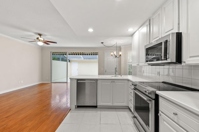 kitchen with a sink, backsplash, white cabinetry, stainless steel appliances, and a peninsula