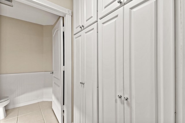 bathroom with a wainscoted wall, toilet, and tile patterned flooring