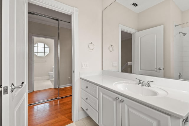 bathroom featuring visible vents, toilet, wood finished floors, a shower, and vanity