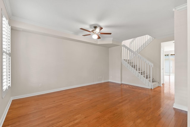 unfurnished living room featuring a ceiling fan, crown molding, light wood finished floors, baseboards, and stairs