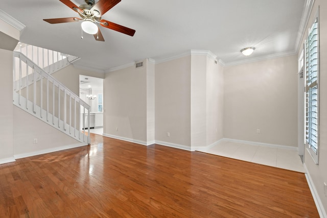 empty room with visible vents, wood finished floors, crown molding, baseboards, and stairs