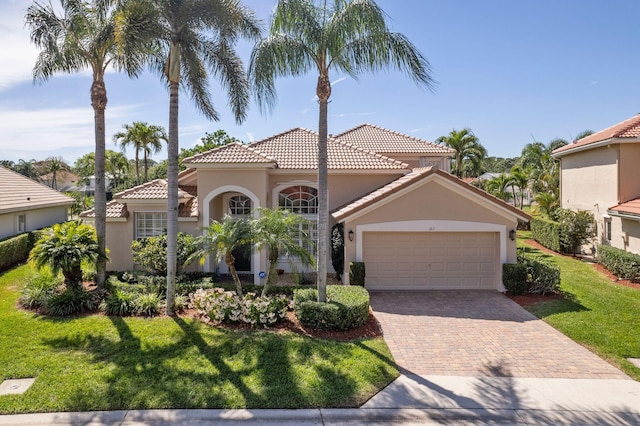 mediterranean / spanish-style house with a front yard, stucco siding, a garage, a tile roof, and decorative driveway