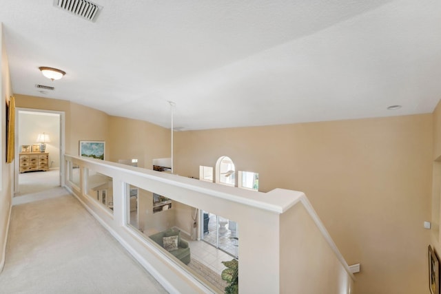 hall featuring visible vents, an upstairs landing, and light colored carpet