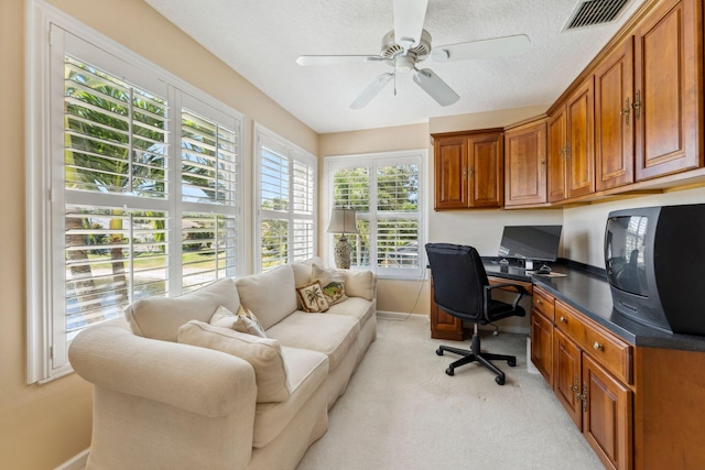 home office featuring a ceiling fan, visible vents, built in study area, a textured ceiling, and light carpet