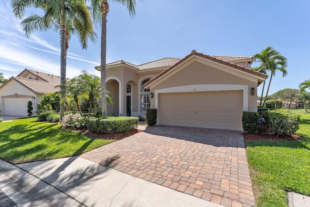 mediterranean / spanish house with a tile roof, a front yard, stucco siding, decorative driveway, and an attached garage