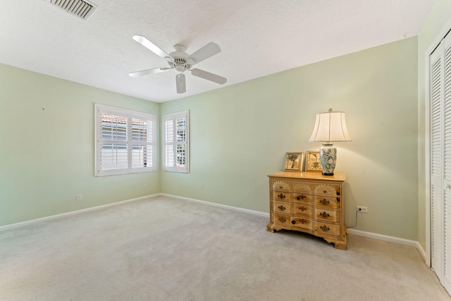 interior space featuring visible vents, baseboards, ceiling fan, light carpet, and a textured ceiling