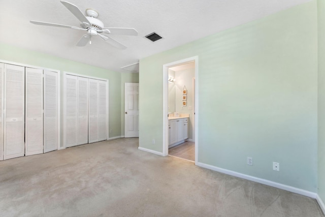 unfurnished bedroom featuring visible vents, baseboards, multiple closets, attic access, and light carpet