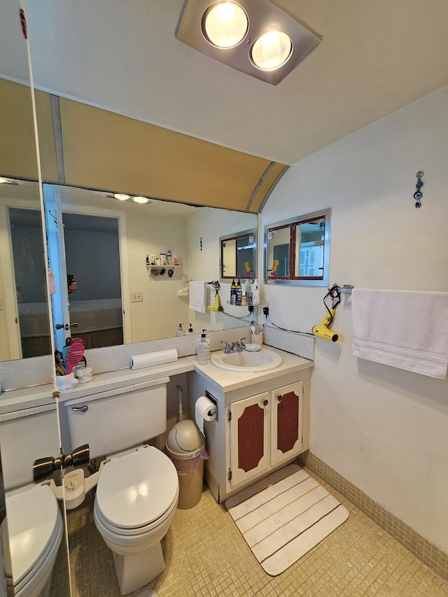 bathroom featuring vanity, vaulted ceiling, toilet, and baseboards