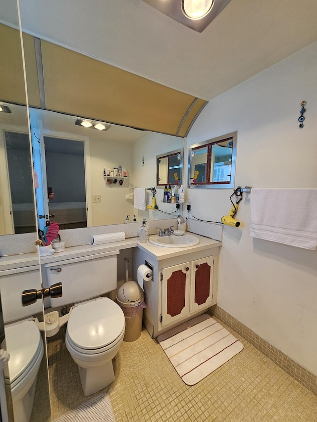 bathroom featuring toilet, vanity, baseboards, and vaulted ceiling