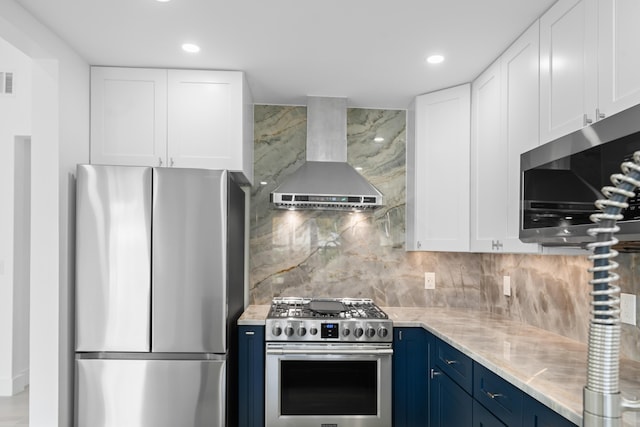 kitchen featuring blue cabinets, appliances with stainless steel finishes, wall chimney exhaust hood, white cabinets, and decorative backsplash