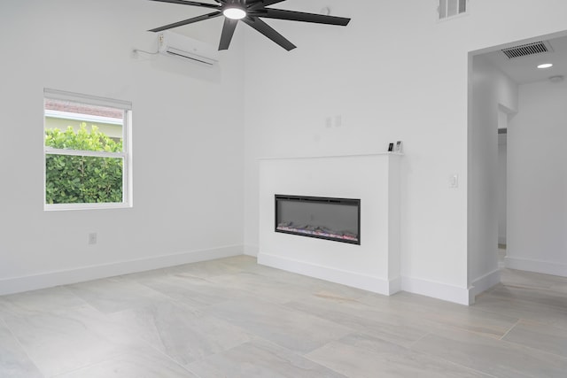 unfurnished living room featuring a glass covered fireplace, a ceiling fan, visible vents, and a wall mounted air conditioner