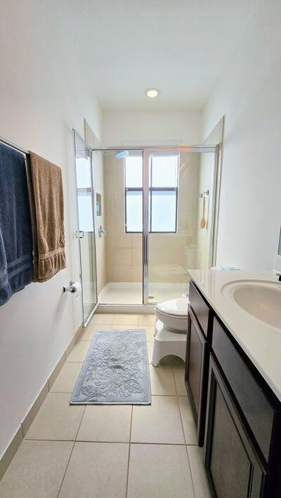 full bath with tile patterned flooring, baseboards, toilet, a stall shower, and vanity