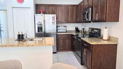 kitchen with dark brown cabinets, light stone counters, appliances with stainless steel finishes, and light tile patterned floors