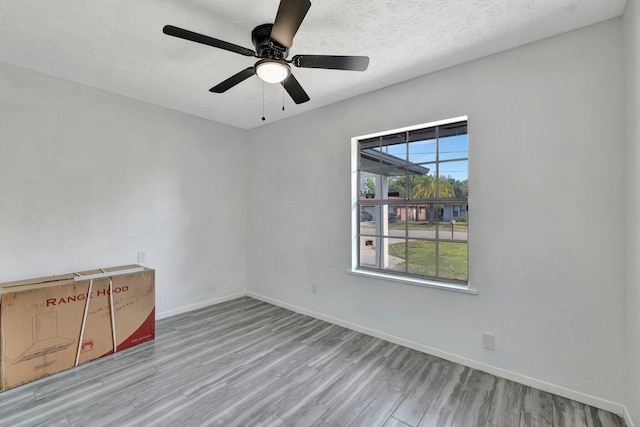 unfurnished room with baseboards, a ceiling fan, a textured ceiling, and wood finished floors