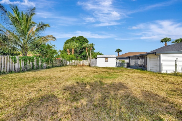 view of yard featuring an outdoor structure, a fenced backyard, a sunroom, a storage unit, and an attached garage