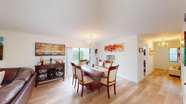 dining area featuring light wood-style flooring, a notable chandelier, and baseboards