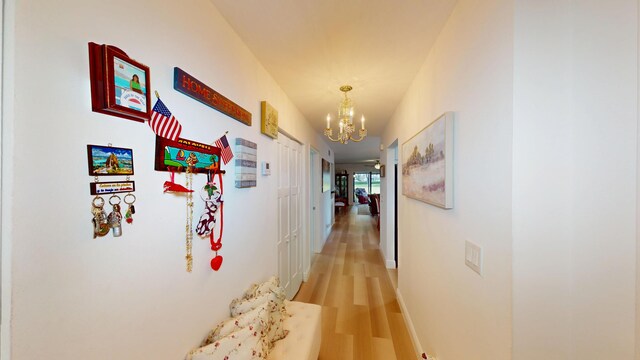 corridor featuring light wood-style flooring, a notable chandelier, and baseboards