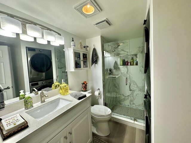 full bath with a marble finish shower, visible vents, toilet, stacked washer and clothes dryer, and wood finished floors