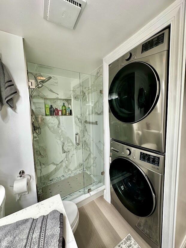 clothes washing area with laundry area, stacked washer and dryer, wood finished floors, and visible vents