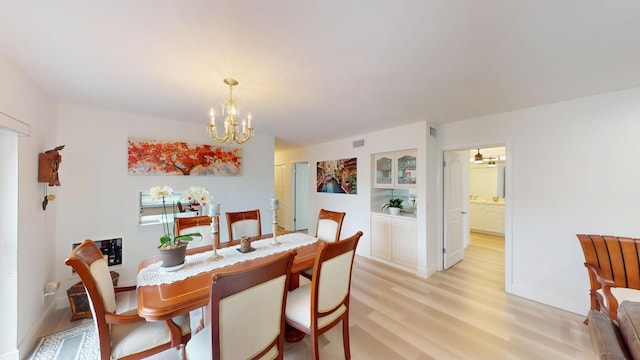 dining space featuring baseboards, visible vents, light wood finished floors, and a chandelier