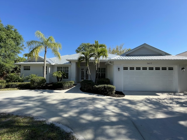 single story home featuring stucco siding, a standing seam roof, concrete driveway, an attached garage, and metal roof