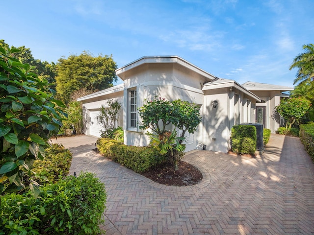 view of side of home featuring decorative driveway, an attached garage, and stucco siding