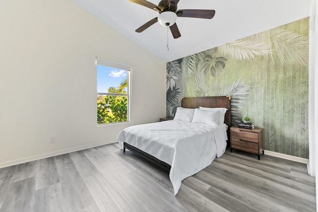 bedroom with wallpapered walls, vaulted ceiling, wood finished floors, an accent wall, and baseboards